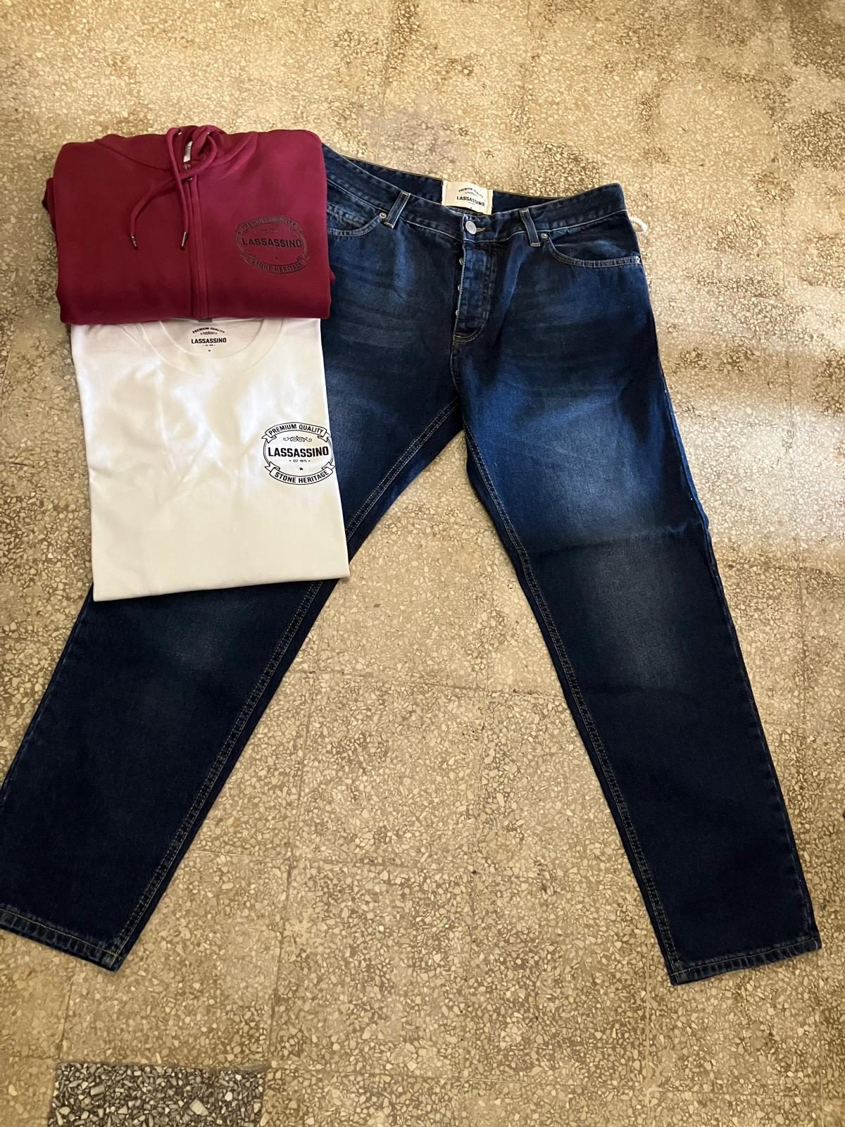 Jeans blu scuro, felpa bordeaux e t-shirt bianca col logo Lassassino Premium Quality Stone Heritage su pavimento in graniglia